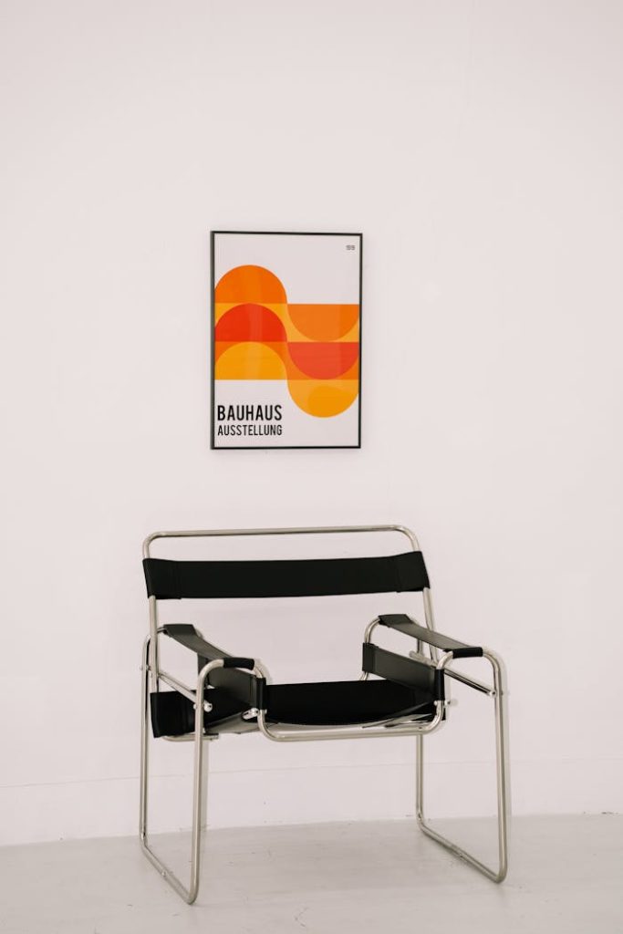 Bauhaus poster with geometric design above a sleek black chair against a white wall.